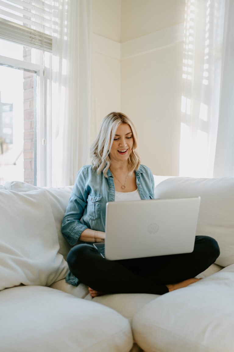 image of Ashley sitting on a white sofa using a laptop